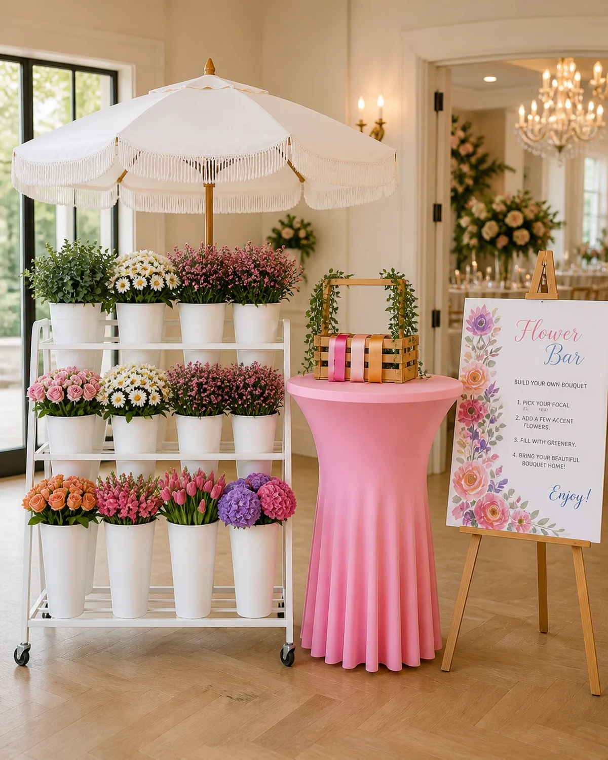 Indoor bloom bar rental setup with white fringe umbrella, pink linen table, and flower stand at an elegant Orange County event venue