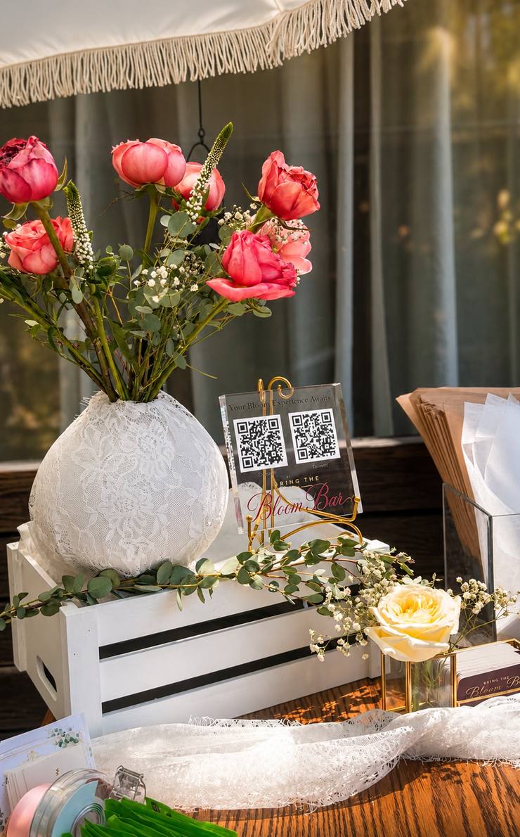 Coral roses and baby's breath in a white lace vase on a styled bloom bar table in Orange County