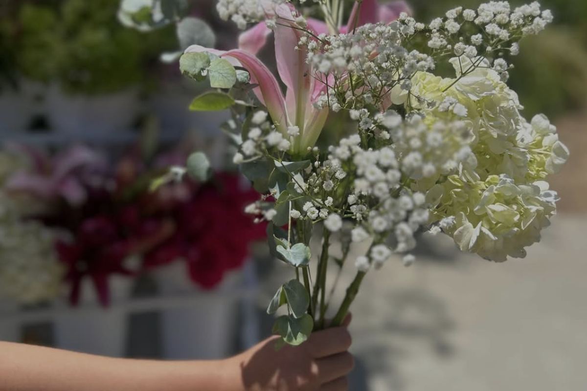 Hand holding a freshly arranged bouquet with baby's breath, pink lily, and white hydrangea at a bloom bar rental